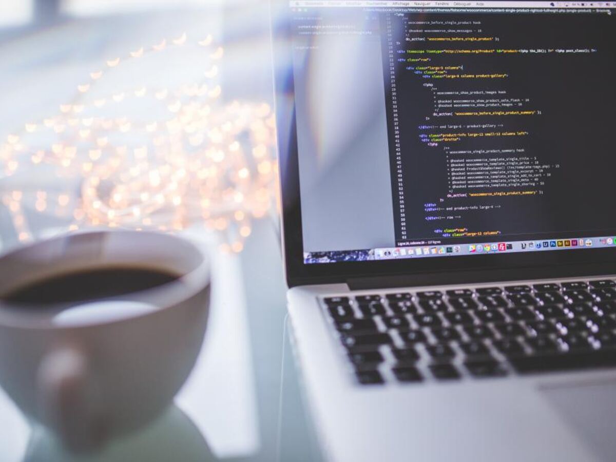A laptop displaying lines of code on a desk beside a cup of coffee